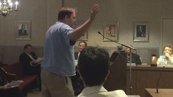 Gator rants at City Council while Mayor Steve catches up on reading in the background
