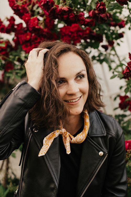 Songwriter and Steph Trivison smiles in a leather jacket and is surrounded by roses.