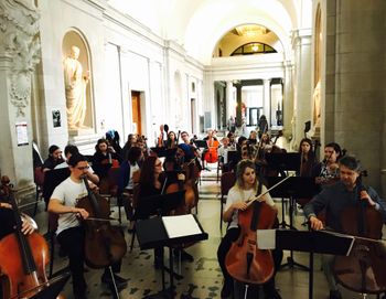 30 cellists warm up in the Great Hall of Carnegie Mellon's College of Fine Arts for the Cello Choir performance
