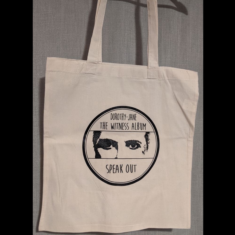 Handy shoulder bag with long 840mm handle. Artwork printed on one side: Dorothy-Jane, The Witness album, SPEAK OUT. Colour: Natural. Dimensions: 300mm x 380mm, Handle 840mm. Thickness 120gsm.