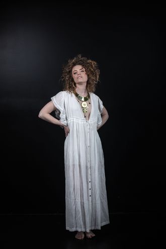 0stella skyward girl standing in white dress grecian white dress nordic celtic bronze age gold necklace torque album cover curly hair sultry stance hands on hips marta mora photography