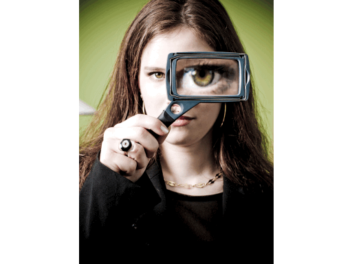 Young woman holds rectangular magnifying glass up to her left eye facing us