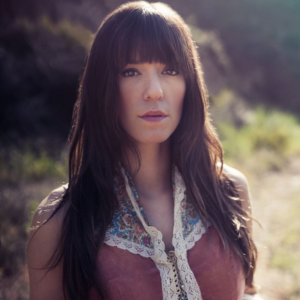 headshot of cassi nicholls wearing a prarie syle dress on a dirt road with wildflowers
