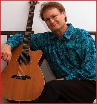 Greg Tamblyn with arm around guitar, each sitting on straight-backed chairs