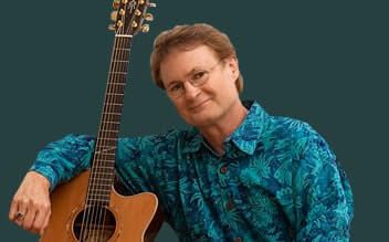 Greg Tamblyn smiling with arm around guitar.