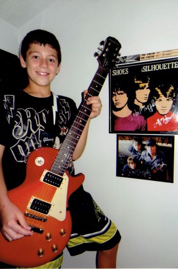 Jimmy shows off his cool Epiphone guitar standing next to his SHOES posters
