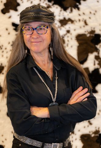 Kristine Best, looking healthy and confident, dressed in a long sleeve black shirt, wearing her trademark cap, black to match of course. Her long hair hangs freely over her shoulders.