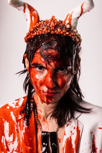 Medusa, trans nonbinary alt-pop musician and rapper; white suit, tuxedo, tiara, horns; bouquet of flowers; fake blood; prom scene, Carrie; photographer Justin Ruggiero
