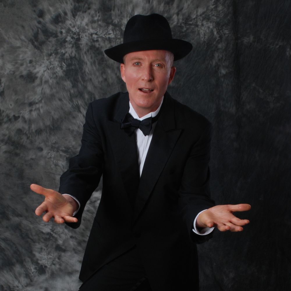 Will McMillan standing in tuxedo with hands outstretched. Photo by Stephen C. Fischer
