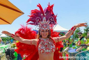 Gorgeous Brazilian dancer of samba posing with arms out and wearing a red and silver feathered costume outdoor at a party
