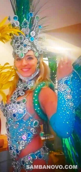 Smiling samba dancer wearing a blue and silver samba costume made of sequins and with a headdress made of green feathers
