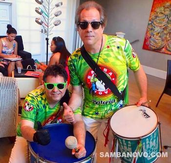 Two handsome samba drummers in green, yellow and red shirts giving the thumbs up before going on stage at an event
