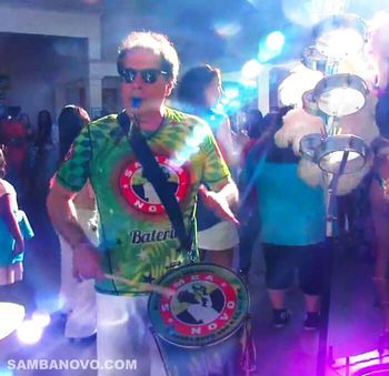Ron DeFrancesco, director and founder of Samba Novo a top entertainment group playing drums with party guests watching
