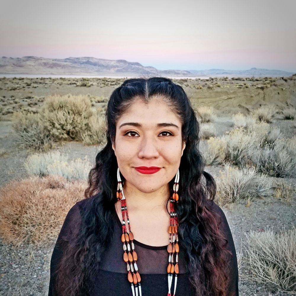 portrait size photo of Indigenous woman facing camera smiling. Background is Pyramid Lake on the Pyramid Lake Paiute reservation in Nixon, Nevada