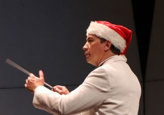 Image: Daniel Hege, a Native American man in white jacket and red Santa hat holding conductor's baton