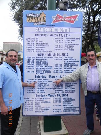 Ruben Jr & Ruben Sr. pointing at the schedule for the 2014 Tejano Music Awards Fan Fair
