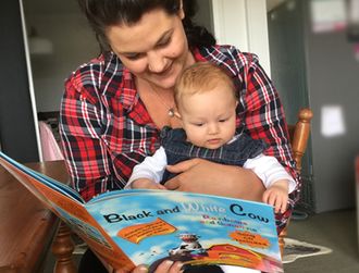 A mum reading the book "Black and White Cow" by Rainbows and Sunshine, to her baby daughter.