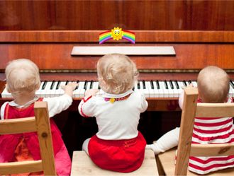 Image of 3 toddlers playing a piano together.