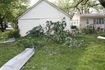 Back side of garage. You can see the power line that has been ripped from the peak of the garage and still hanging on the right side. Plus all the limbs and tin.