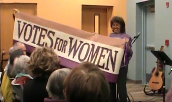 Sharleen Leahey holding replica of tri-color Woman's Suffrage banner during "Give The Ballot To The Mothers," the final song at the end of Act I of "Songs of Woman's Suffrage Centennial Concert" performed on March 25, 2017 at the Boardman Road Library in Poughkeepsie, NY