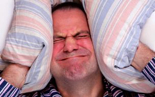 Image-of-grimacing-man-holding-pillows-to-his-ears