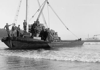 A barge...laden with gum......'shippies' west coast Northland.... about to to pulled out through those waves by the steamer in the distance
