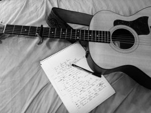 Notepad, pen and guitar laying on a bed following a songwriting session.