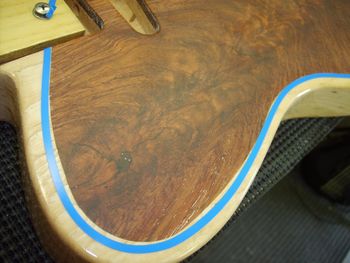 I've taped off a smooth curve around the walnut inlay, and will sunburst the inside edge. This will even out any inconsistencies in the compound curve.