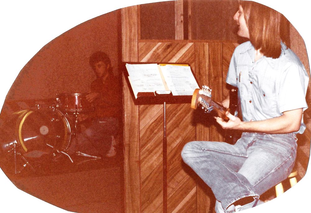 Rick Richards setting up his drums while Bruce serenades him on a Fender 12-string guitar, November 1981