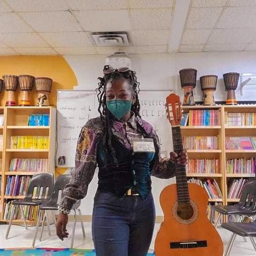 Malaika Avi in classroom smiling and holding guitar