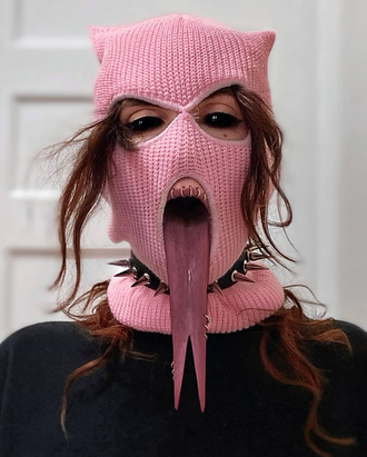 Medusa, non-binary musician; pop artist; rapper; hip-hop artist; pink balaclava, black eyes, foot long forked tongue, pierced; spiked collar. brown waves pouring out of ski mask.