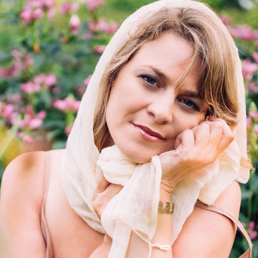 Anic Asha (Anic Proulx) avec un regard doux. Fichu sur la tête en lin blanc beige avec des fleurs roses délicates à l'arrière.