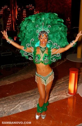 Hire samba dancers like this dancer who is posing with her hands outstretched in a green costume made of feathers