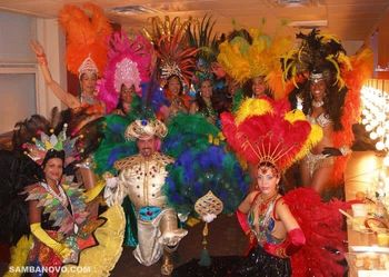 A group of 9 samba dancers in very colorful feathered costumes posing proudly backstage at Radio City Music Hall