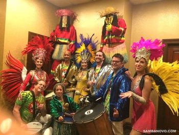 Nine members of the Samba Novo band posing together after a samba show, 3 dancers, 5 drummers and 2 moco jumbies