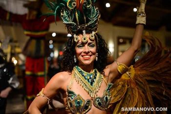 A Samba dancer in a green & gold sequin costume raising her hand in celebration at the end of a wedding reception performance
