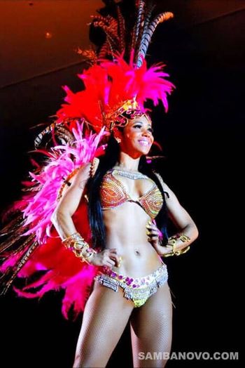 Gorgeous samba dancers for hire near me in a pink, red, and gold Brazilian bikini standing with hands on hips after performing at an event