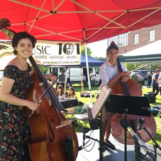 two classical musicians smiling under a tent while playing at a Melrose MA music festival organized by TIMKO