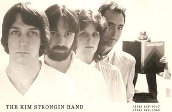 The Kim Strongin Band Official 8x10 glossy. Left to right: Keith Hurrell, drums; Mike Guido, bass; Kim Strongin, guitar,vocals; Douglas Baldwin, guitar, vocals. In the background, reading the book on Ancient Egypt: Paul Shields.
