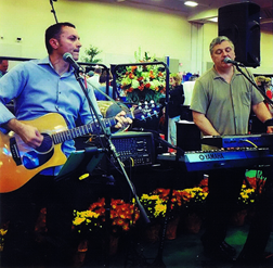 Sandy Vine Acoustic Duo performing on a flowered stage for a convention trade show wine social at the Niagara Falls Scotiabank Convention Centre.