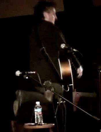 Screen capture from a videotape of my opening set for Dave Alvin at the Acoustic Music San Diego Concert Series at the Normal Heights Methodist Church.  Here I am mid-jump at the end of my rave-up on “Dollars To Dust” to end the show.  Video by Kurt Mahoney
