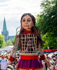 Magnolia Sisters with youth orchestra play music for the arrival of the 12 ft high puppet, Little Amal