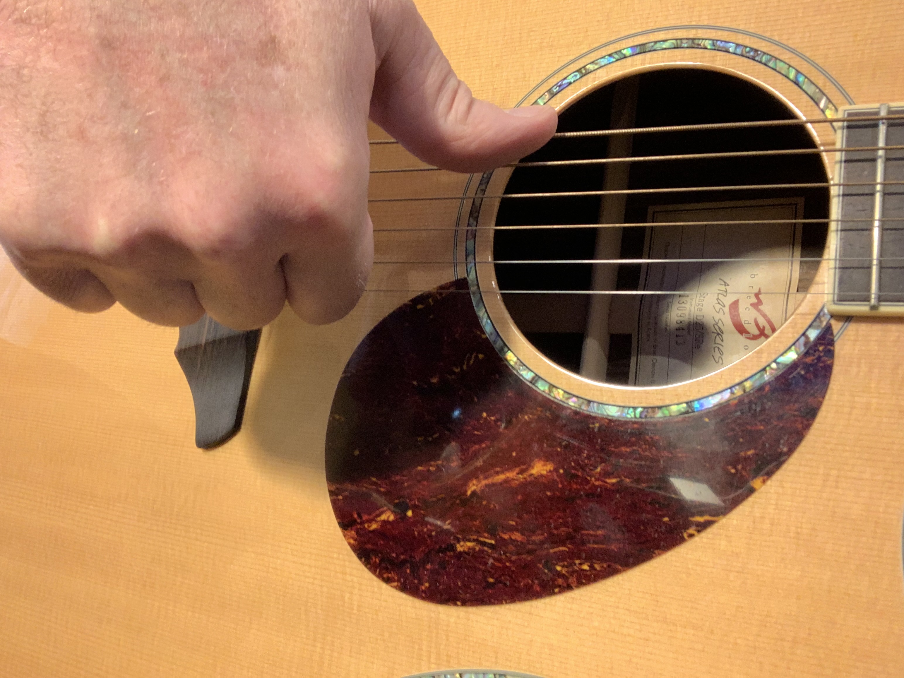 Close up of a guitar teacher showing placement of right hand thumb on low e string of guitar