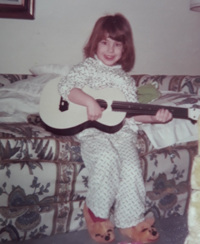 grainy photo from nineteen seventies of a young girl with a child's guitar and winnie the pooh slippers