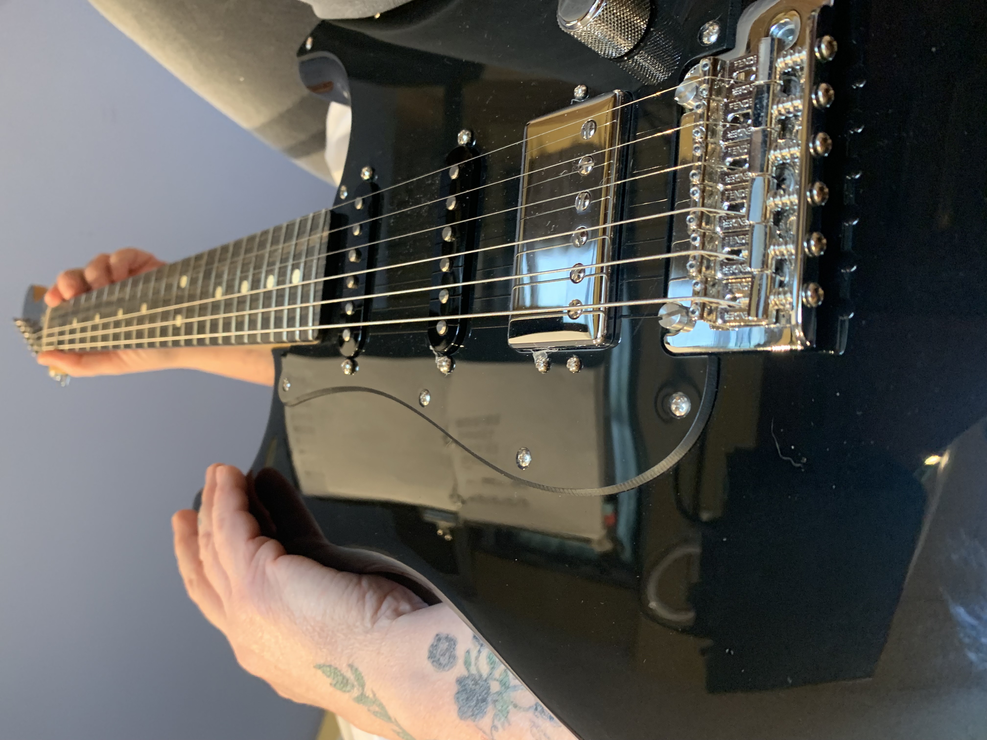 Student of Songdog Music with arm tattoos holding her guitar, a black fender Stratocaster