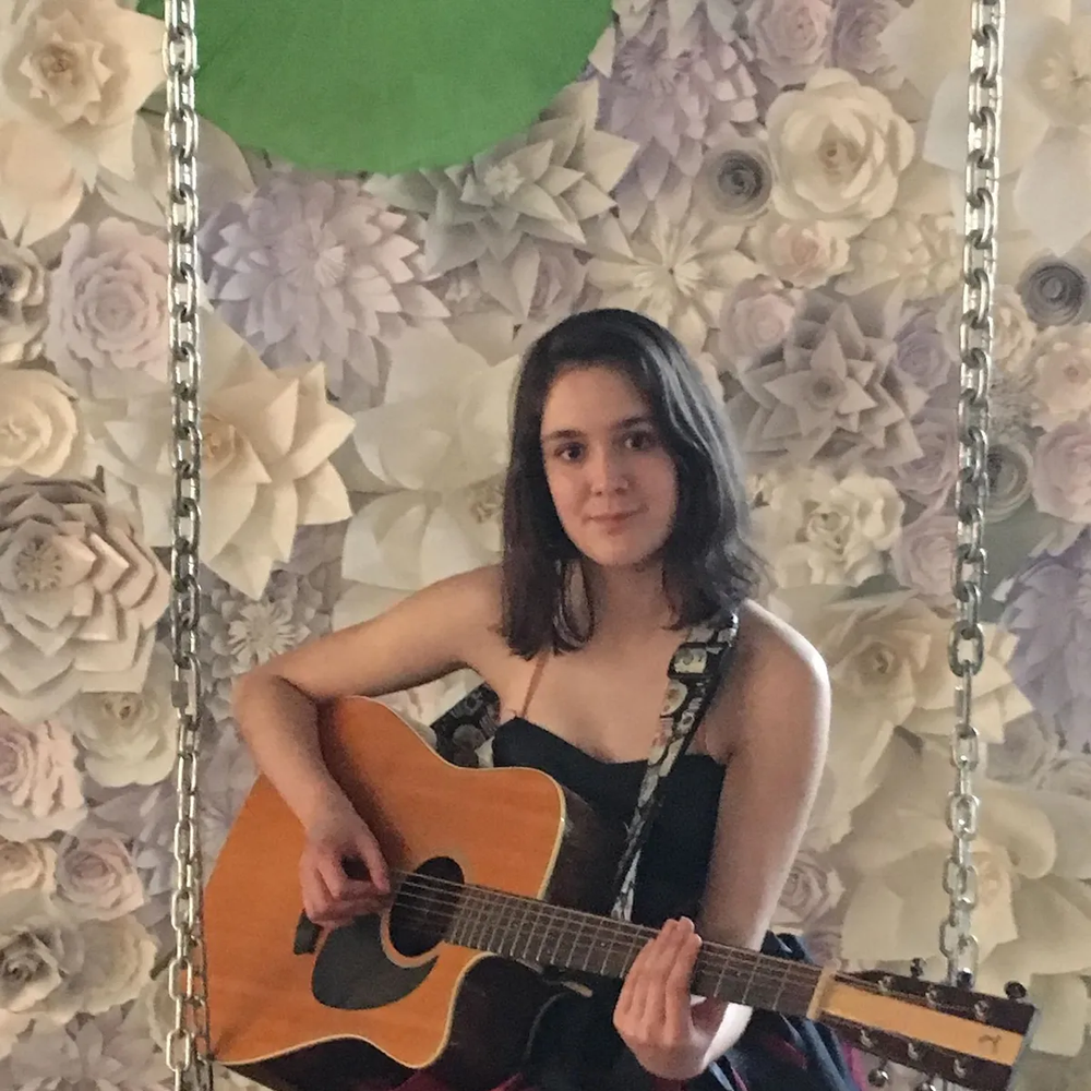 Portrait of a Young girl smiling at the camera whilie holding a guitar with a flowery background behind her