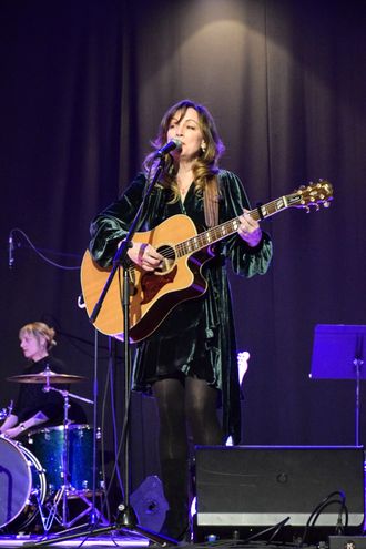 Tara MacLean sings into a mic holding a guitar