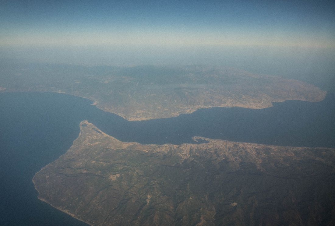 The southern Italian coast (top left), the Strait of Sicily, and the island of Sicily (bottom right) photographed from the airplane to Rome. Coast Guard ships holding hundreds of migrants commonly disembark in ports along these coasts.
