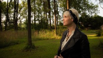 Woman looking left outside in a wooded setting.
