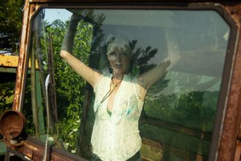 Woman inside a combine cab looking outside at camera.
